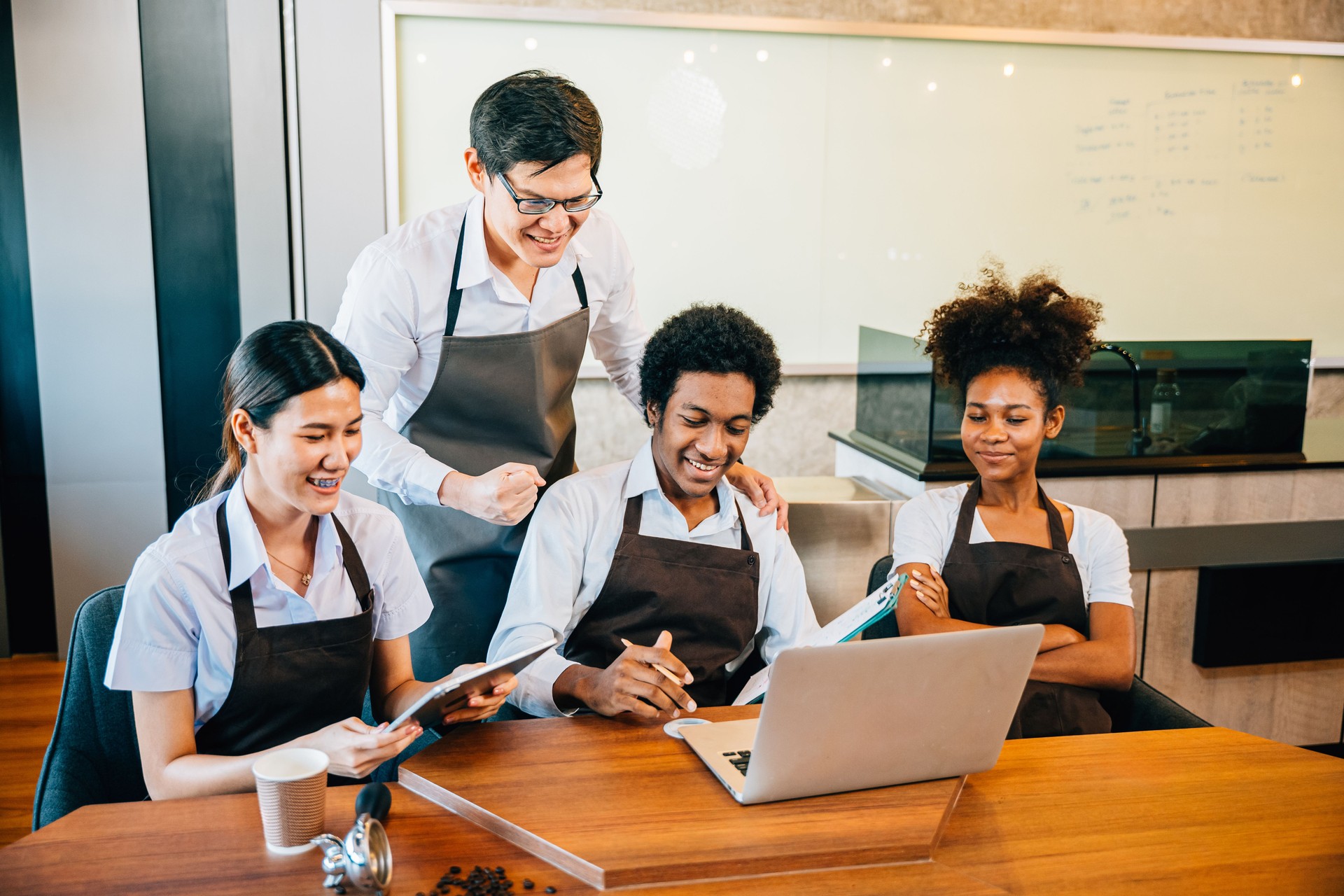 Diverse entrepreneurs in stylish coffee shop have a team meeting. Barista owner discuss work on laptop. Multiethnic employees successful teamwork business discussion.